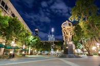 城市广场充满活力，夜空下引人注目的雕塑被周围的建筑和郁郁葱葱的绿化所环绕