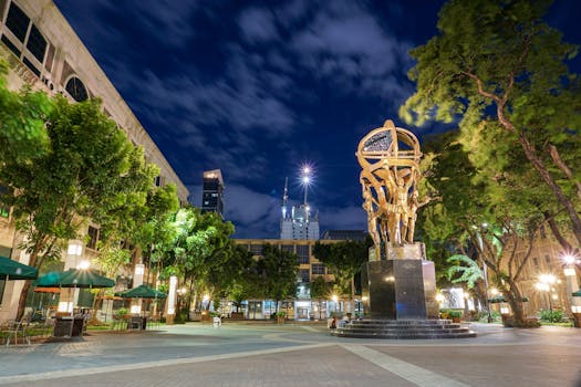 城市广场充满活力，夜空下引人注目的雕塑被周围的建筑和郁郁葱葱的绿化所环绕