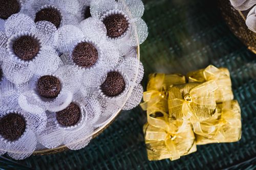 Free Top view of brigadeiros with sprinkles in decorative white wrappers beside wrapped yellow gifts on a textured surface. Stock Photo