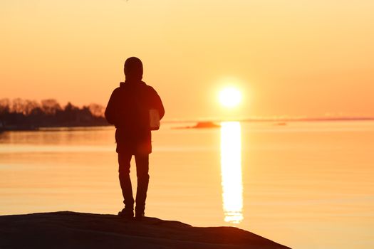 A serene scene of a person meditating by the water during a winter sunrise at Cove Island Park, Stamford.