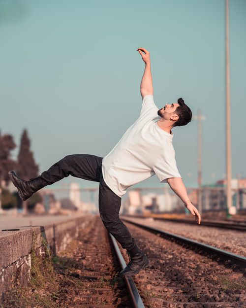 Free Man in casual pose balancing on railway tracks with a clear day background. Stock Photo