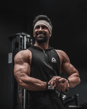 Smiling muscular man flexing arms in gym wearing black athletic wear and headband.