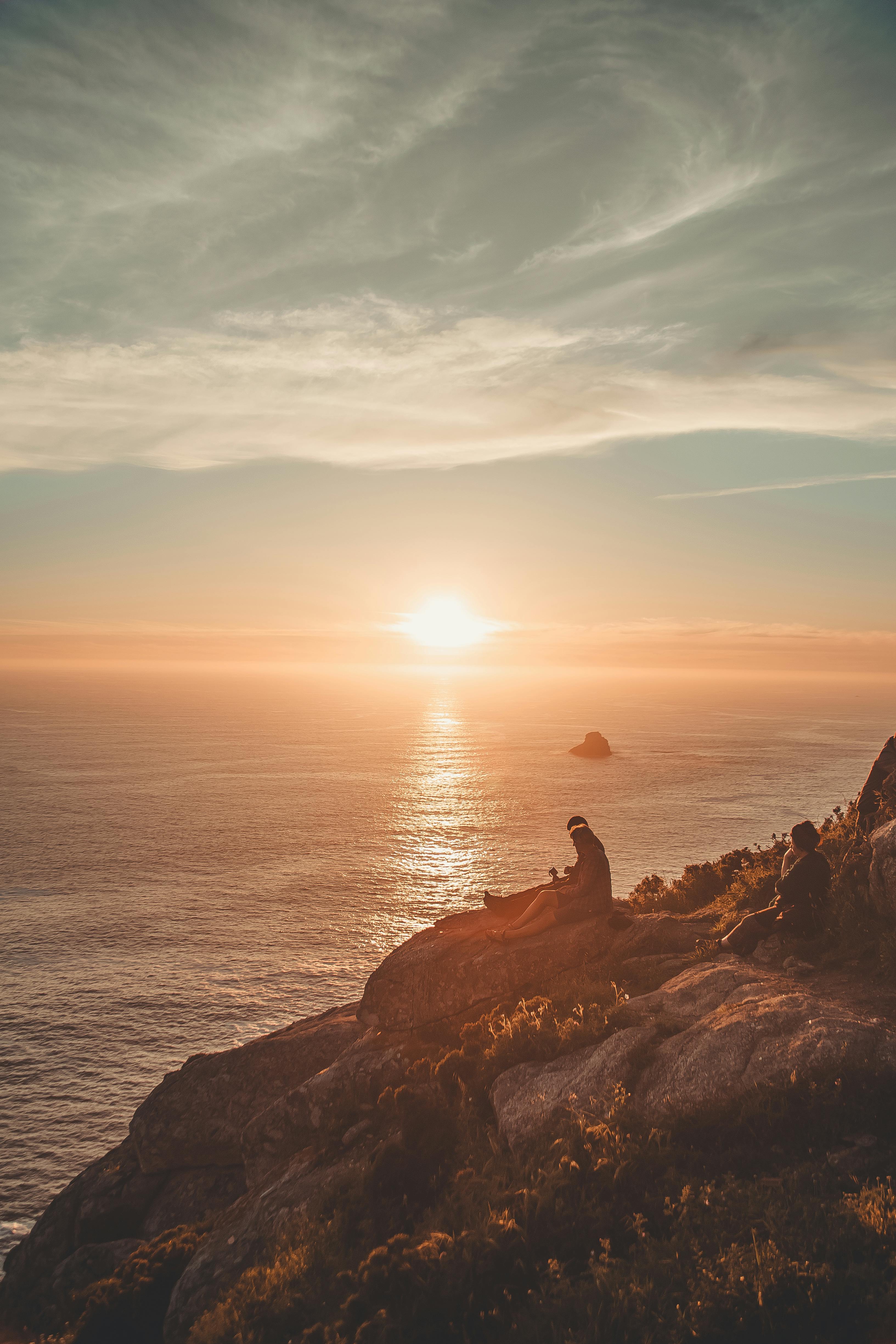 日落时分，一个人坐在沿海的悬崖上，凝望着海天相接的地平线