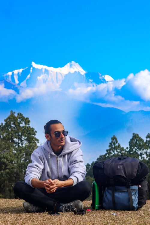 Free Young man seated with a backpack, enjoying the view of the Himalayas in Nepal. Stock Photo