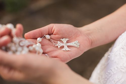 Free Close-up of a bride's hand holding a cross necklace, symbolizing faith and love. Stock Photo