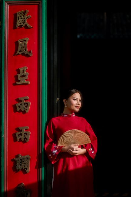 A woman in a red traditional dress holds a fan beside ornate Chinese signage, creating a cultural and elegant ambiance.