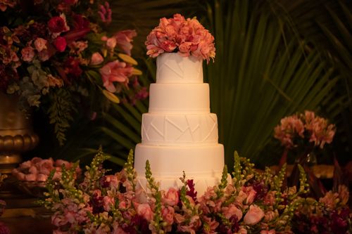 Free A stunning four-tier wedding cake adorned with pink flowers, surrounded by lush greenery. Stock Photo