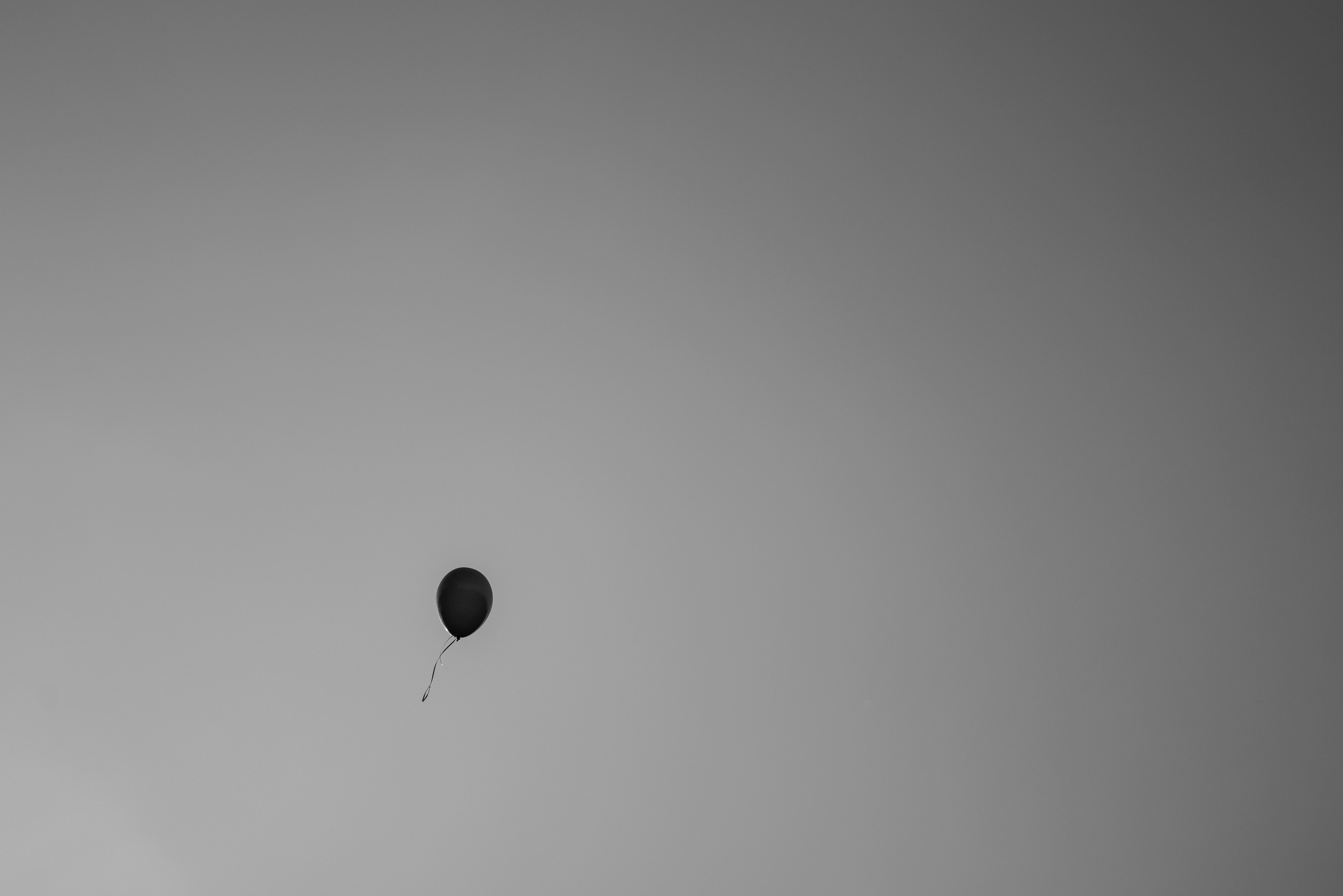 Bezpłatne Pojedynczy czarny balon unoszący się na szarym, minimalistycznym niebie, symbolizujący samotność. Zdjęcie z galerii