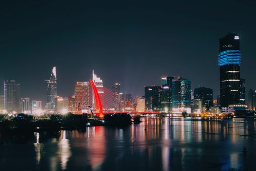 A vibrant nighttime view of the illuminated Ho Chi Minh City skyline reflecting on the river.
