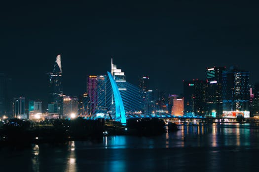 Vivid nighttime view of a cityscape featuring an illuminated bridge and skyscrapers reflecting on the water.