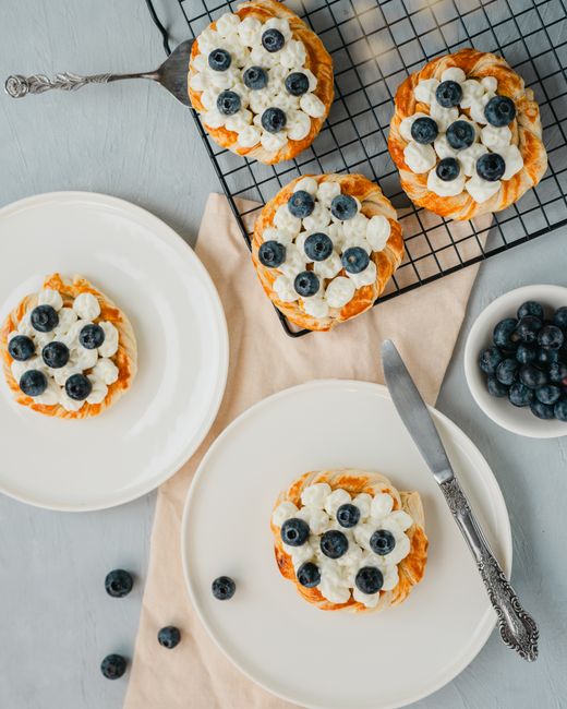 Freshly baked blueberry tarts with cream cheese frosting arranged on a table for a delightful snack.
