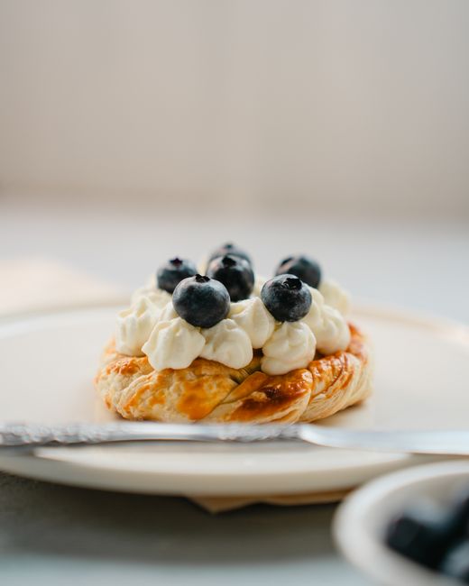 A blueberry-topped pastry with cream served on a white plate, perfect for dessert lovers.