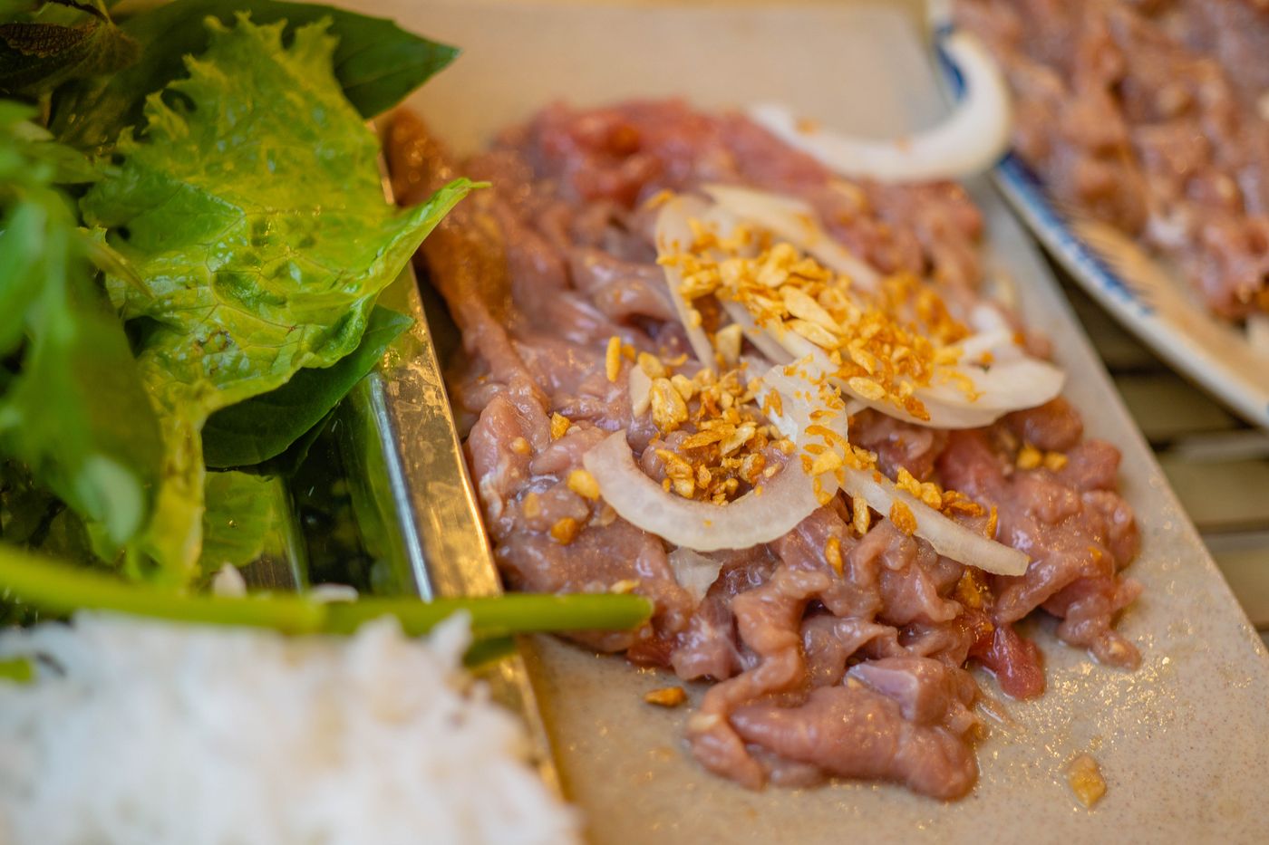 Raw meat garnished with onions and spices, served with fresh greens for a flavorful meal.