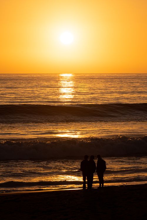 Free A couple silhouetted against a vibrant sunset over the ocean, creating a serene and romantic atmosphere. Stock Photo
