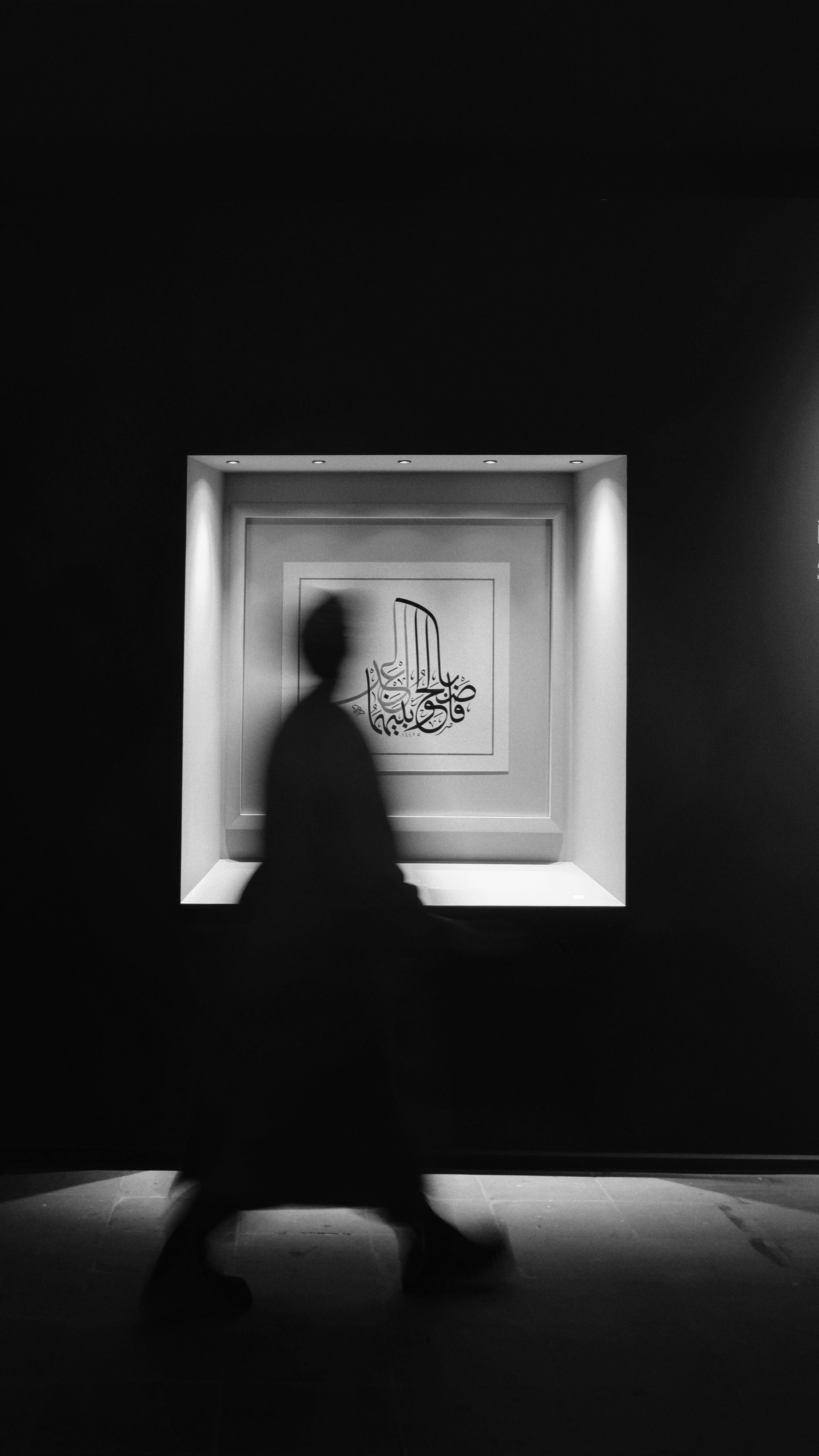 Gratis Una silueta borrosa camina junto a una obra de arte enmarcada e iluminada en una habitación oscura. Foto de stock