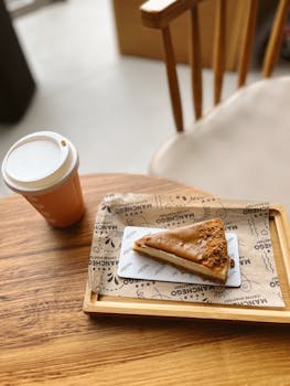 Slice of caramel cheesecake with a coffee cup in a cozy cafe setting.