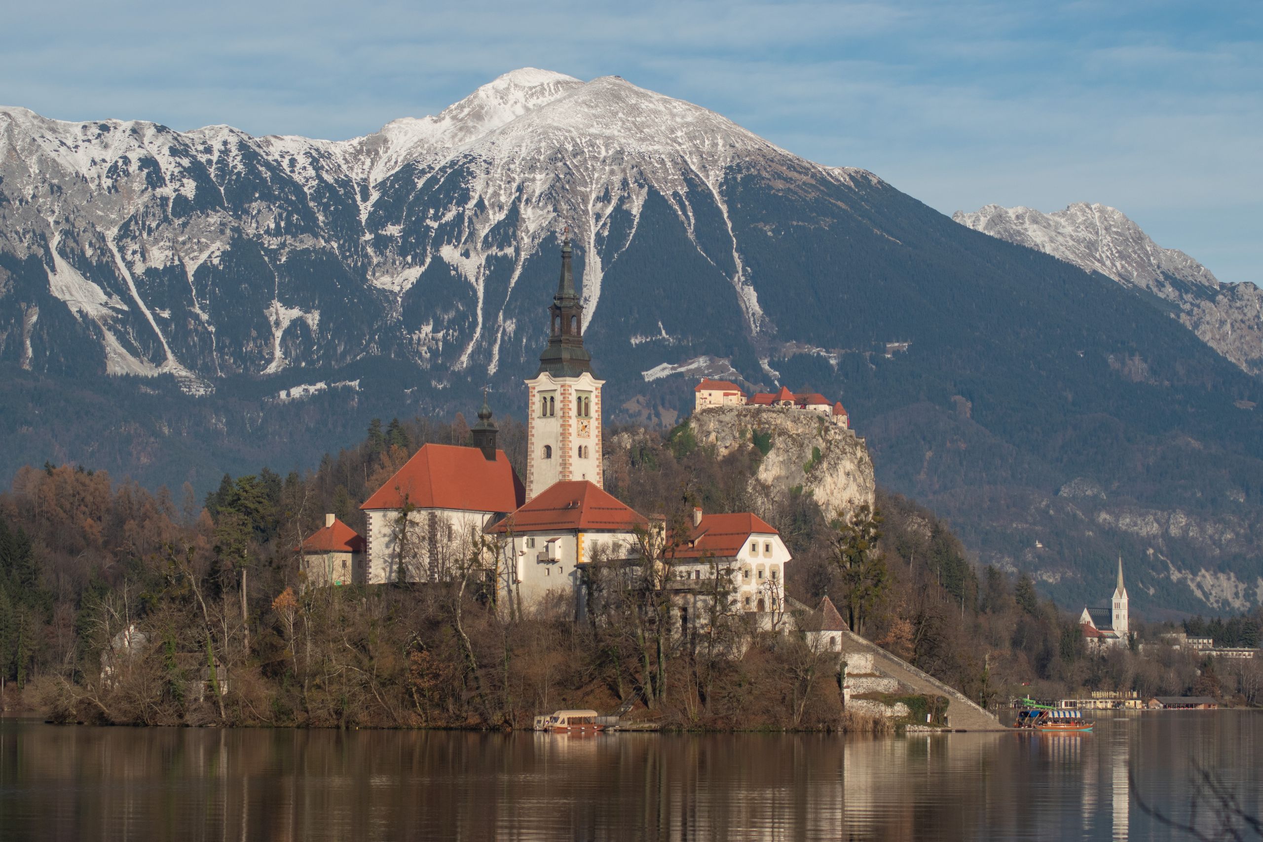 Pulau Bled dengan gereja beratap merah dan Kastil Bled di tebing, latar Pegunungan Alpen, Danau Bled, Slovenia