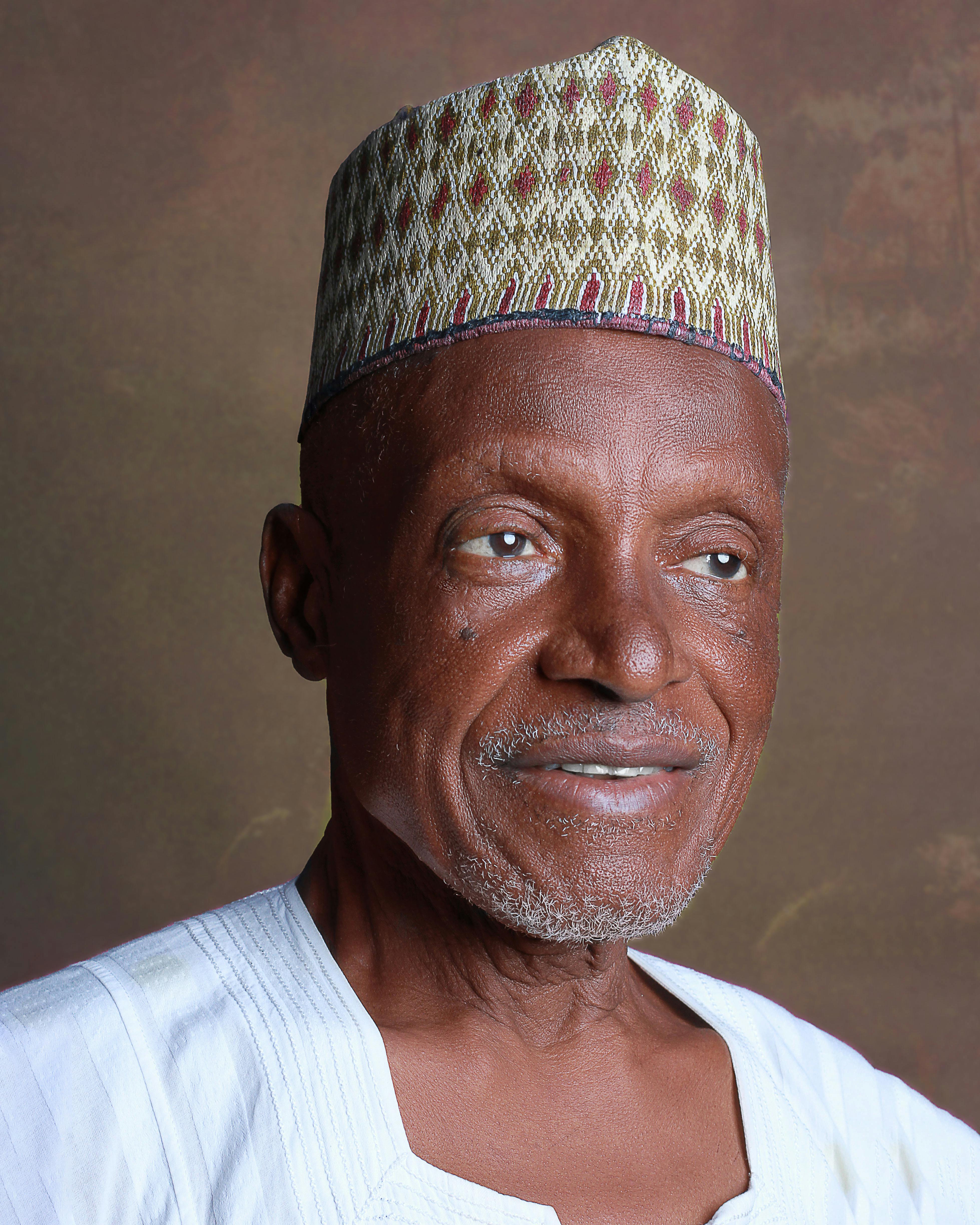 A senior man wearing a traditional hat and attire, smiling warmly.