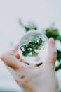 一只手小心翼翼地握住一个反射绿叶的玻璃球，营造出梦幻般的视觉效果