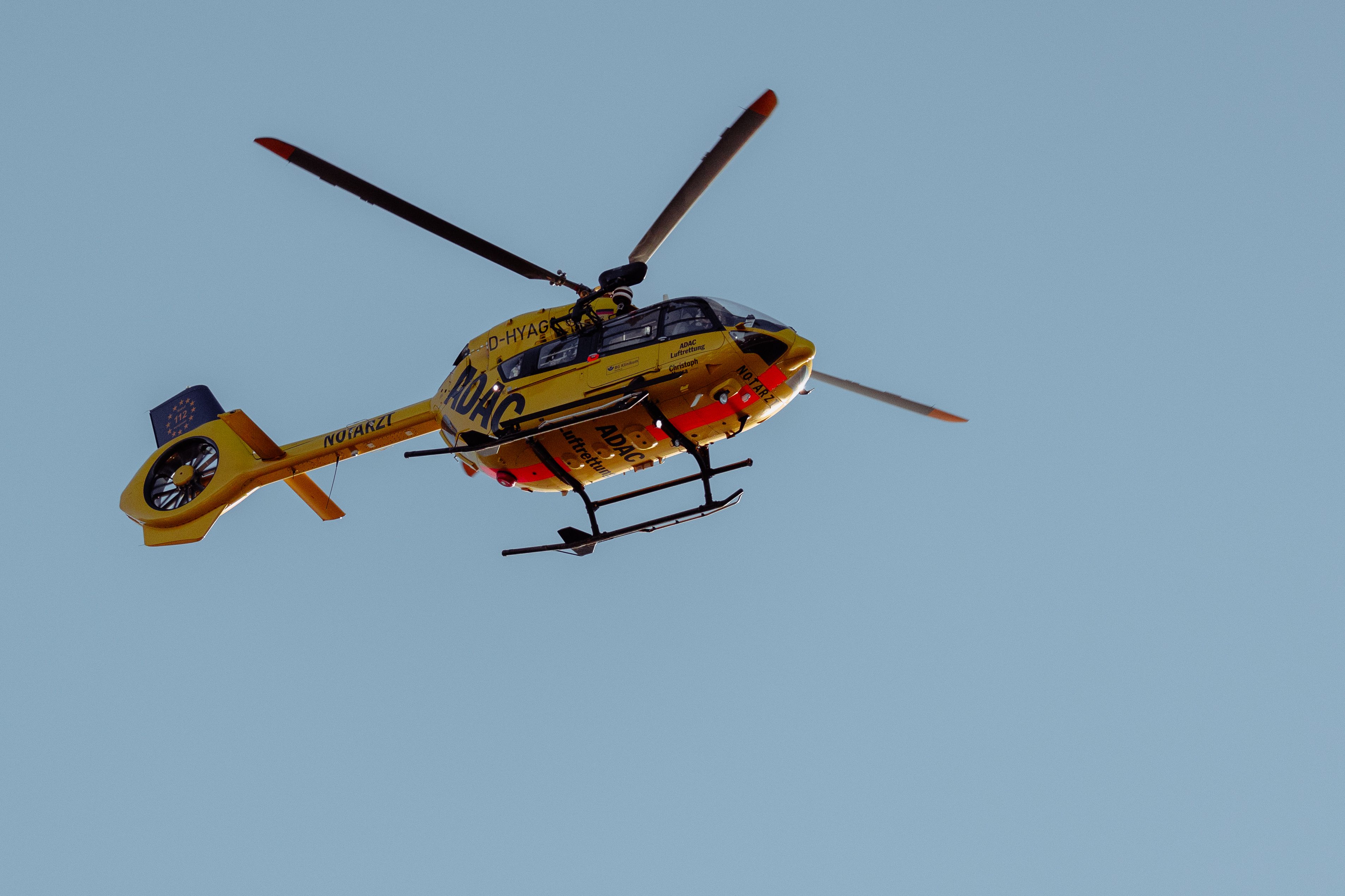 A yellow rescue helicopter flying in a clear blue sky.