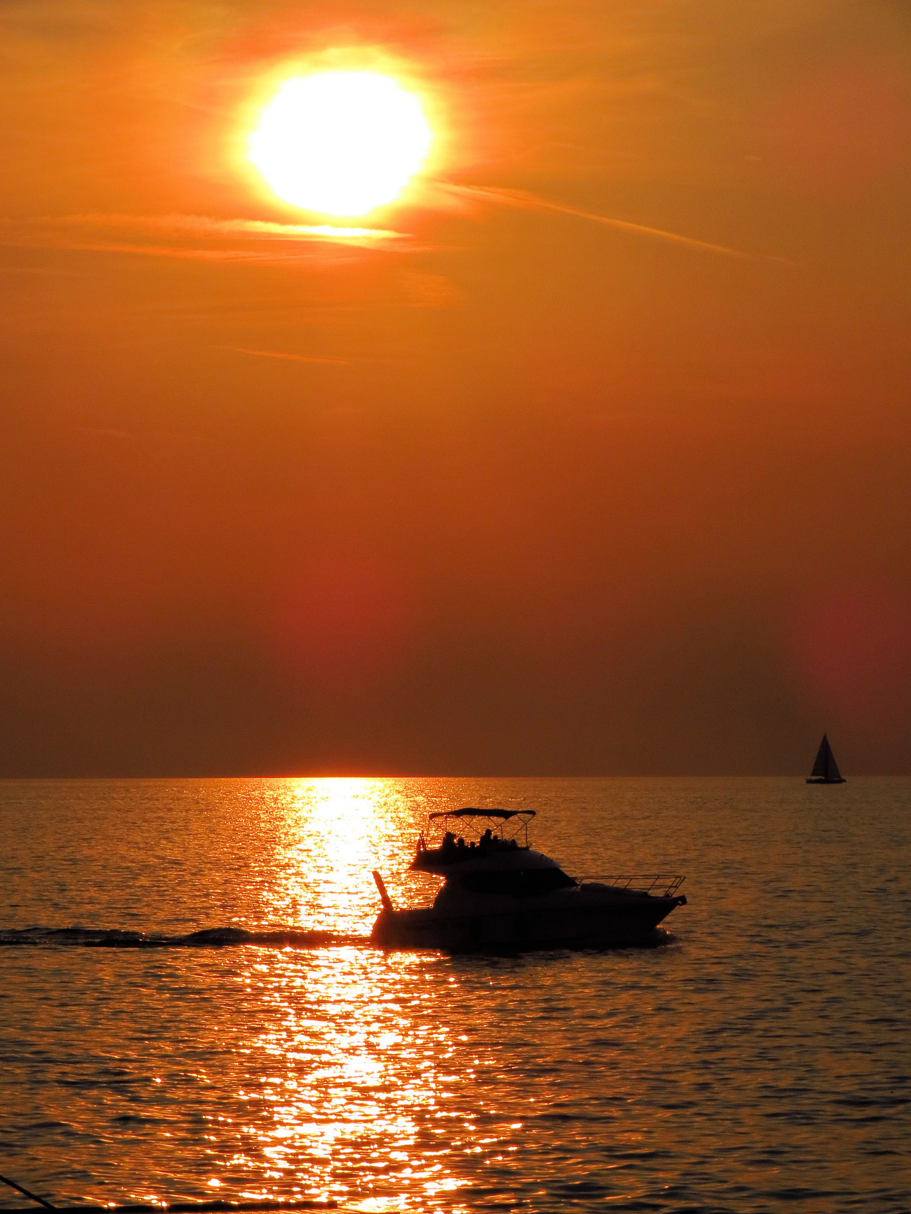 Silhouette of a boat navigating at sunset over calm ocean waters with vibrant orange sky.