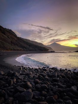 Experience the serene sunset over the volcanic black sand beach with Mount Teide in the background.