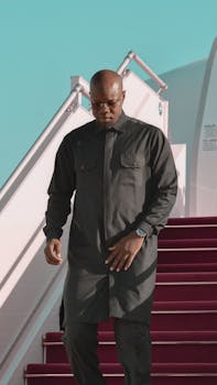 Person in formal clothing walking down airplane stairs, daylight setting.