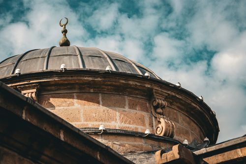 Free A beautifully detailed mosque dome silhouetted against a clear blue sky with white clouds. Stock Photo