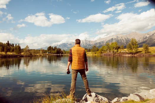 在加拿大艾伯塔省坎莫尔，一名男子站在宁静的湖边，眺望着远处的山景