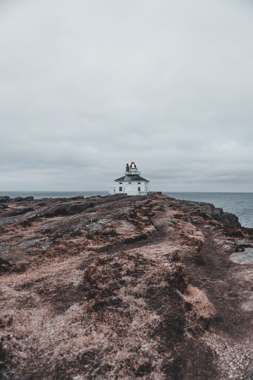 Free A solitary lighthouse stands on a rugged rocky shore under a moody, overcast sky. Stock Photo