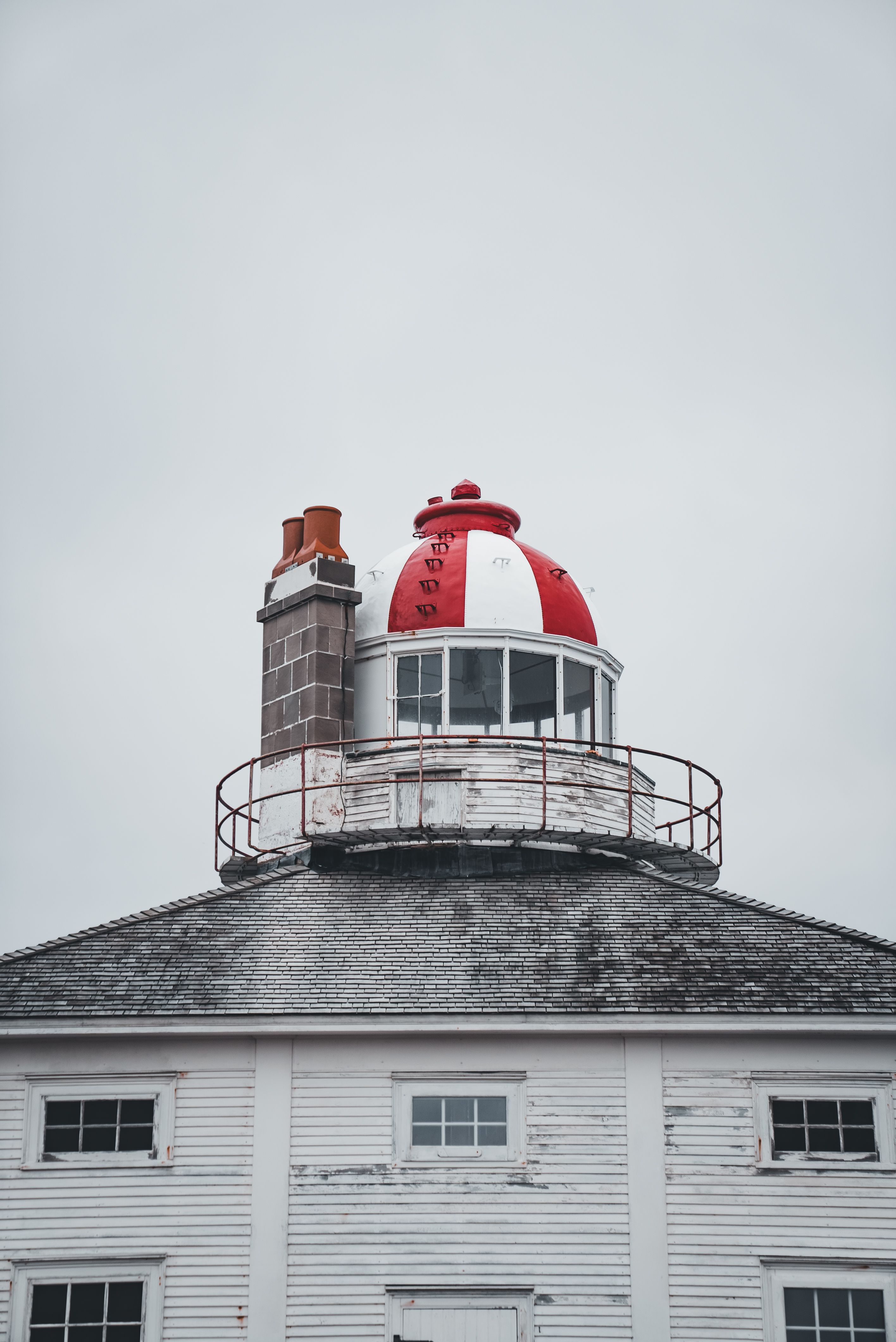 A historic lighthouse with a distinctive red and white dome stands towering against a cloudy sky.