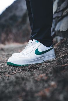 Close-up of white sneakers with a green logo on an outdoor path.