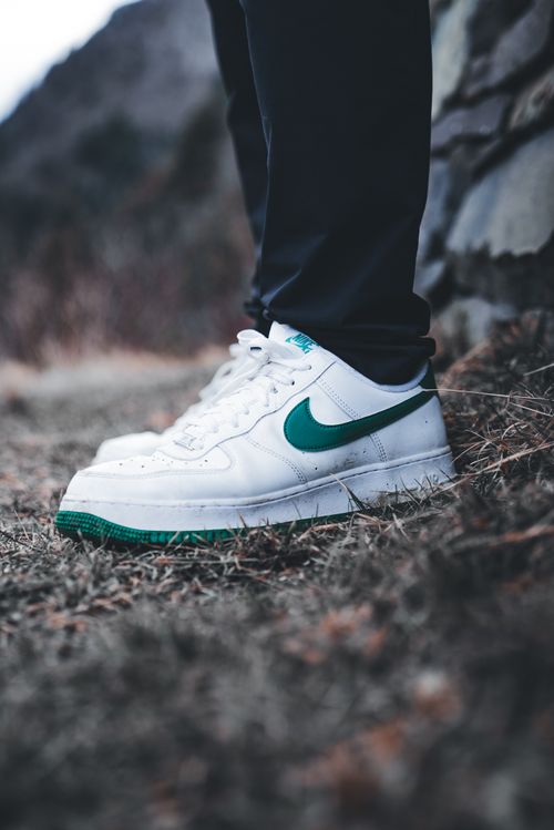 Free Close-up of white sneakers with a green logo on an outdoor path. Stock Photo