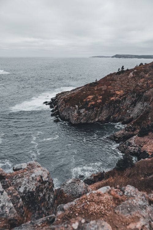 Free Breathtaking view of rugged coastal cliffs meeting the ocean under a cloudy sky. Stock Photo