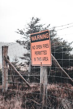 Photo by Erik Mclean Warning sign against open fires in forested area with fence and trees, creating a clear safety message.