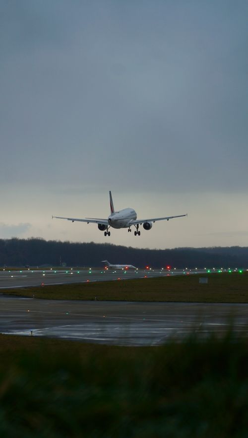 Free A commercial airplane descends onto a runway with guiding lights at dusk, capturing travel and aviation themes. Stock Photo