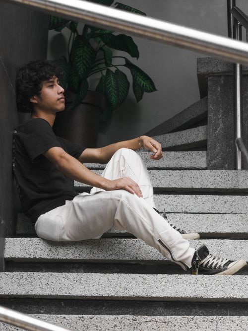 Free A young man in casual wear sitting on stairs indoors with plants around. Stock Photo