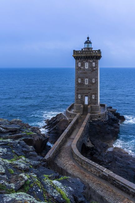 Beautiful lighthouse on Brettagne's rocky coast with waves crashing around.