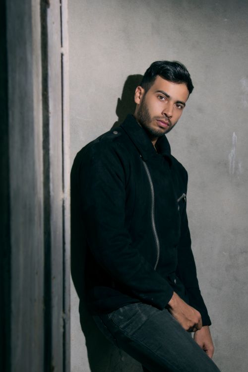 Free Portrait of a fashionable young man in a dark jacket leaning against a wall. Stock Photo