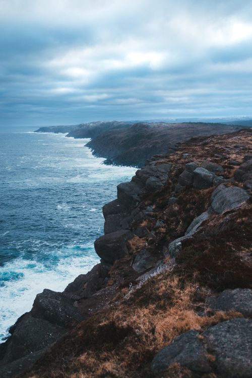 Free Spectacular view of a rugged coastline with dramatic cliffs and ocean waves under an overcast sky. Stock Photo