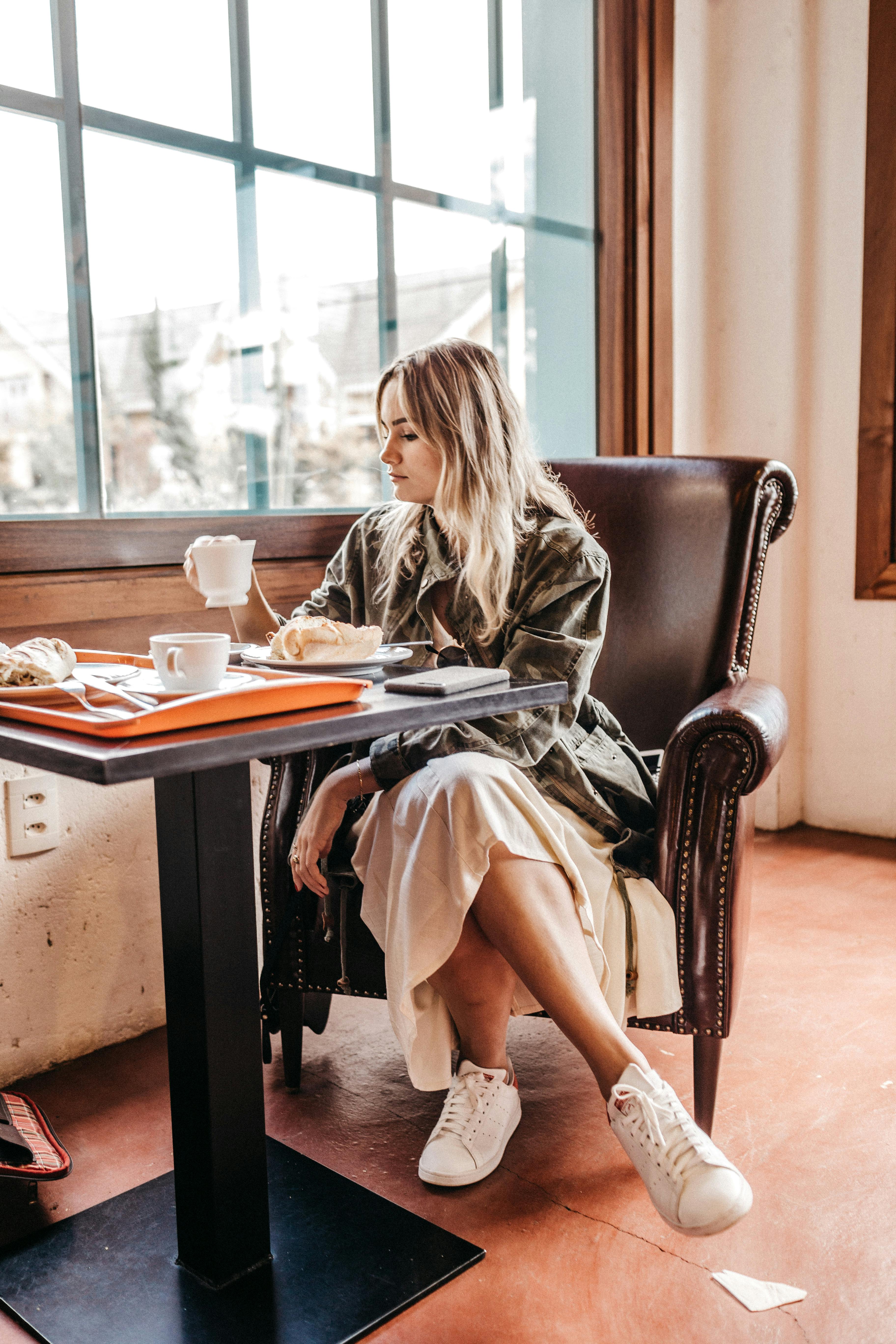 一位时尚女性坐在咖啡馆舒适的窗前，享用着咖啡和糕点