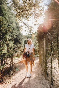 A fashionable woman exploring a sunlit forest pathway in casual attire, radiating style.