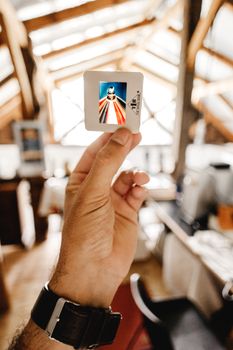 An adult hand holding a vintage photo slide with a vibrant image indoors.