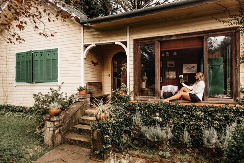 Free A serene scene of a woman reading by the window of a quaint, ivy-covered cottage. Stock Photo