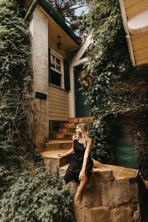 Free Stylish woman in black sitting on rustic outdoor steps surrounded by greenery. Stock Photo