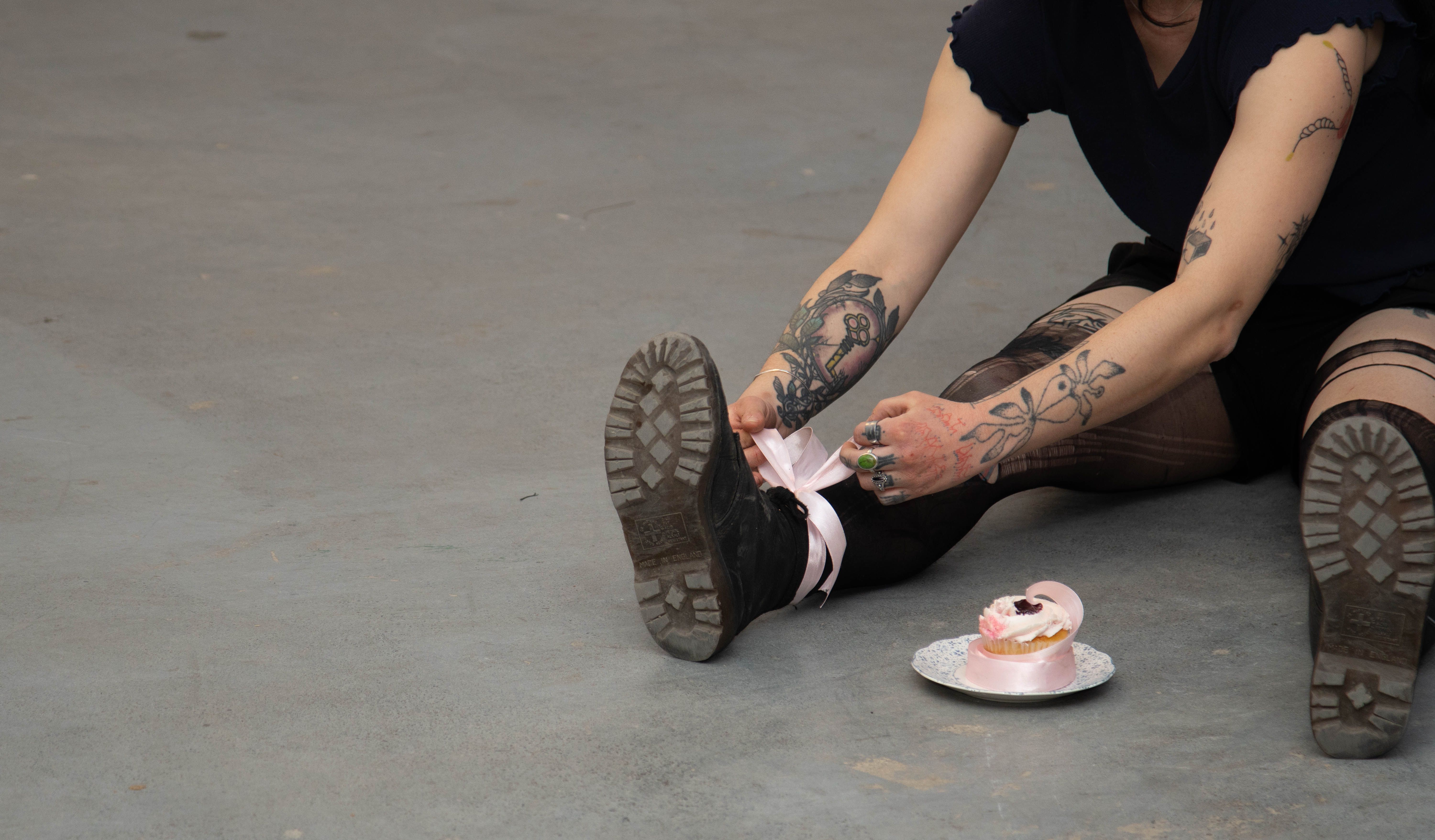 Tattooed person in Montreal tying shoes beside a pink-frosted dessert dish.