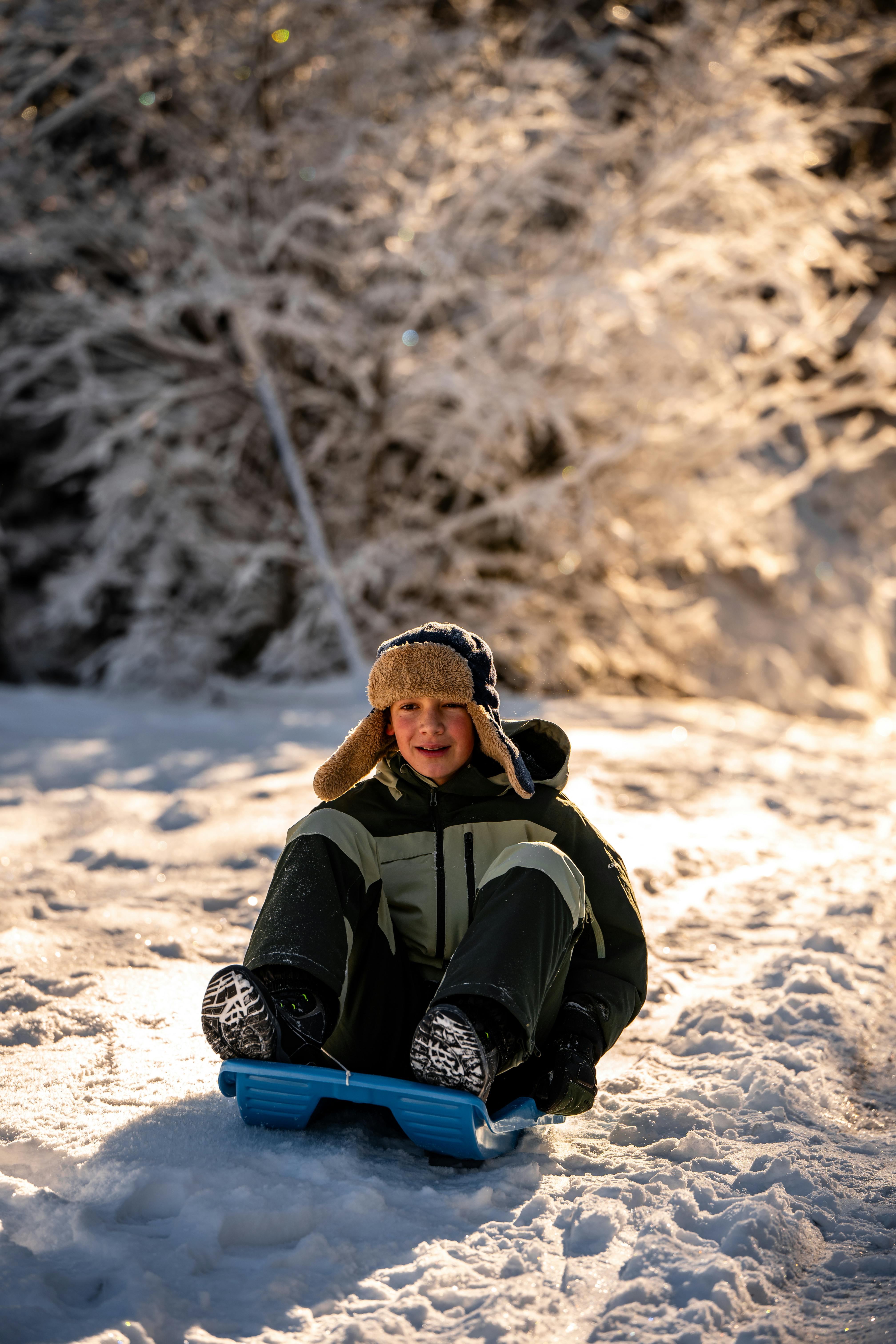 A child joyfully sledding down a snowy hill during a sunny winter day in Planica, Slovenia.