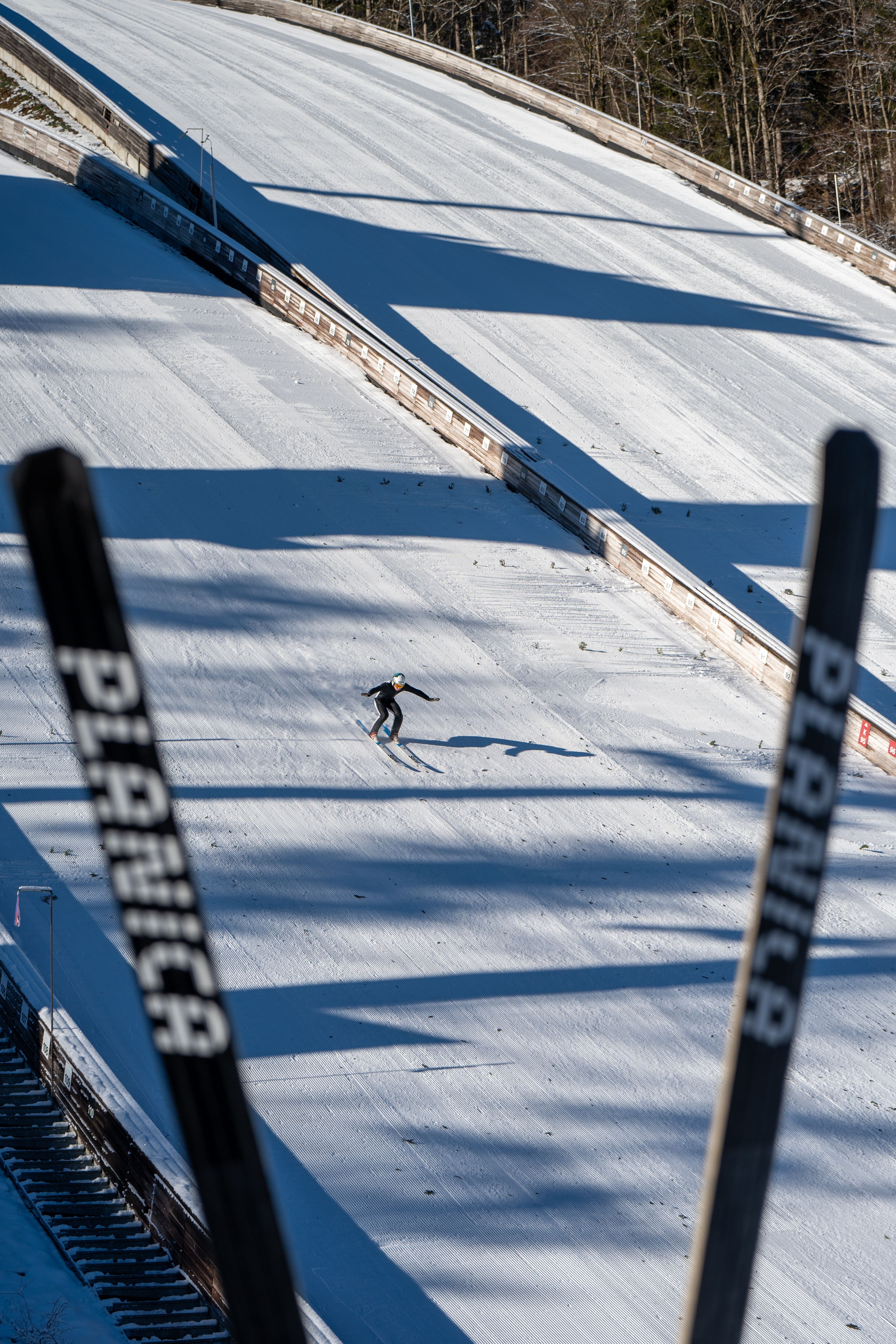 A skier navigates the snowy slopes of Planica, Slovenia, captured between ski jump towers.