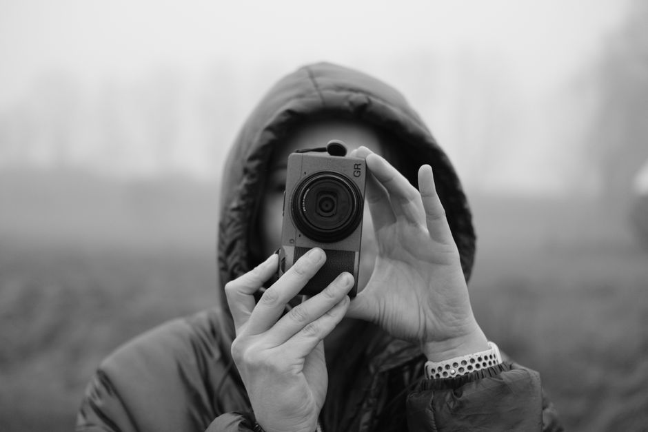Close-up of a photographer in a hood, holding a camera on a foggy day.