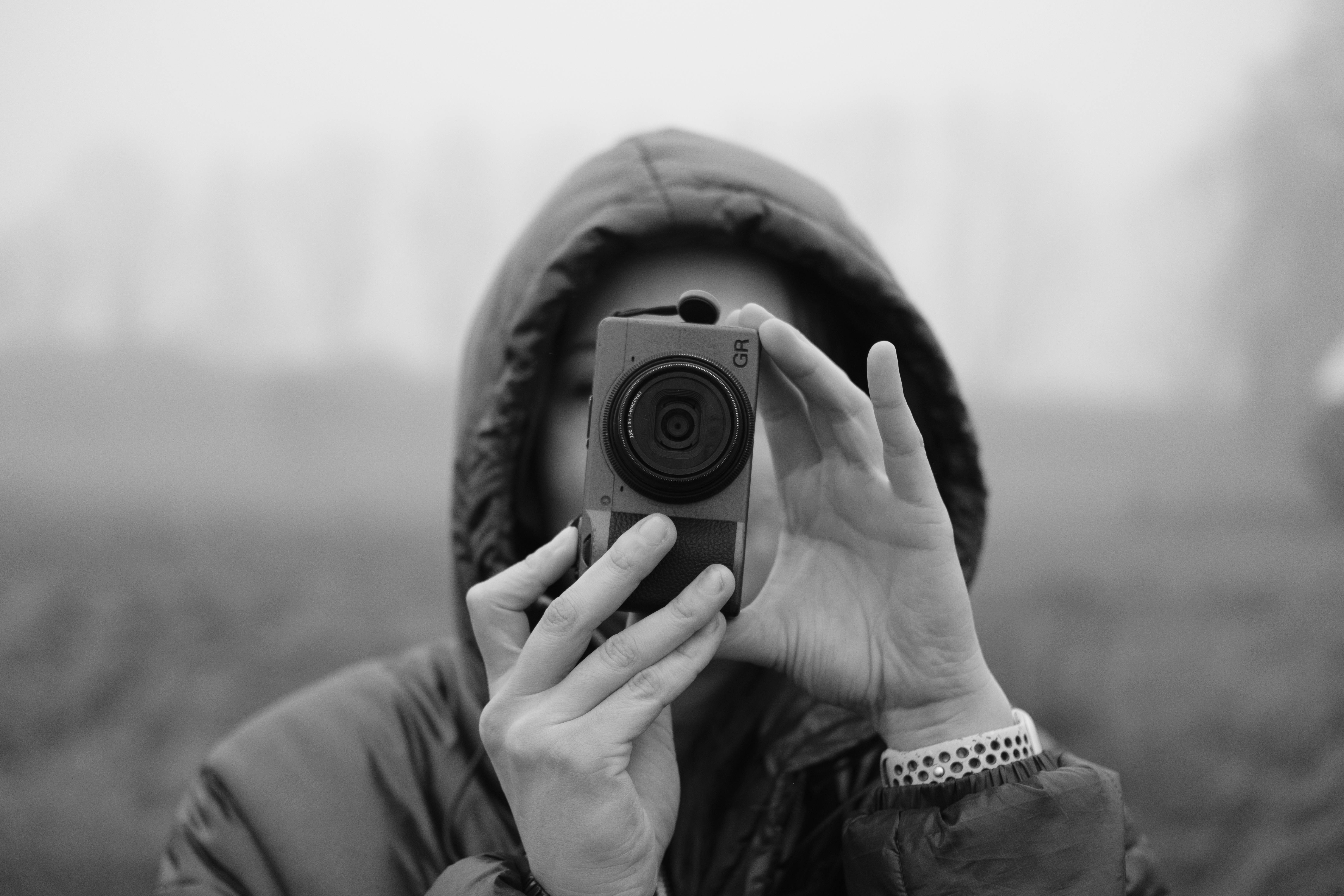 Gratis Primer plano de un fotógrafo con capucha, sosteniendo una cámara en un día de niebla. Foto de stock